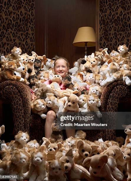 girl sitting in an armchair full of stuffed toys - eccesso foto e immagini stock