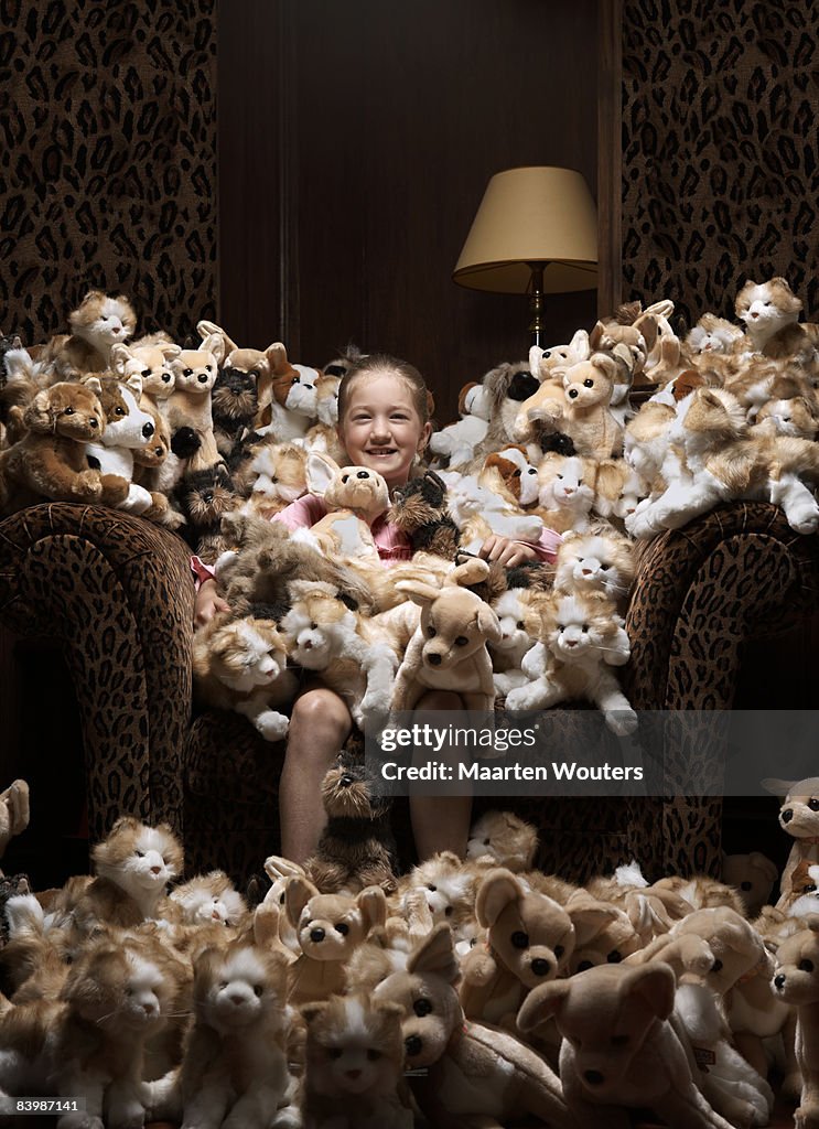 Girl sitting in an armchair full of stuffed toys