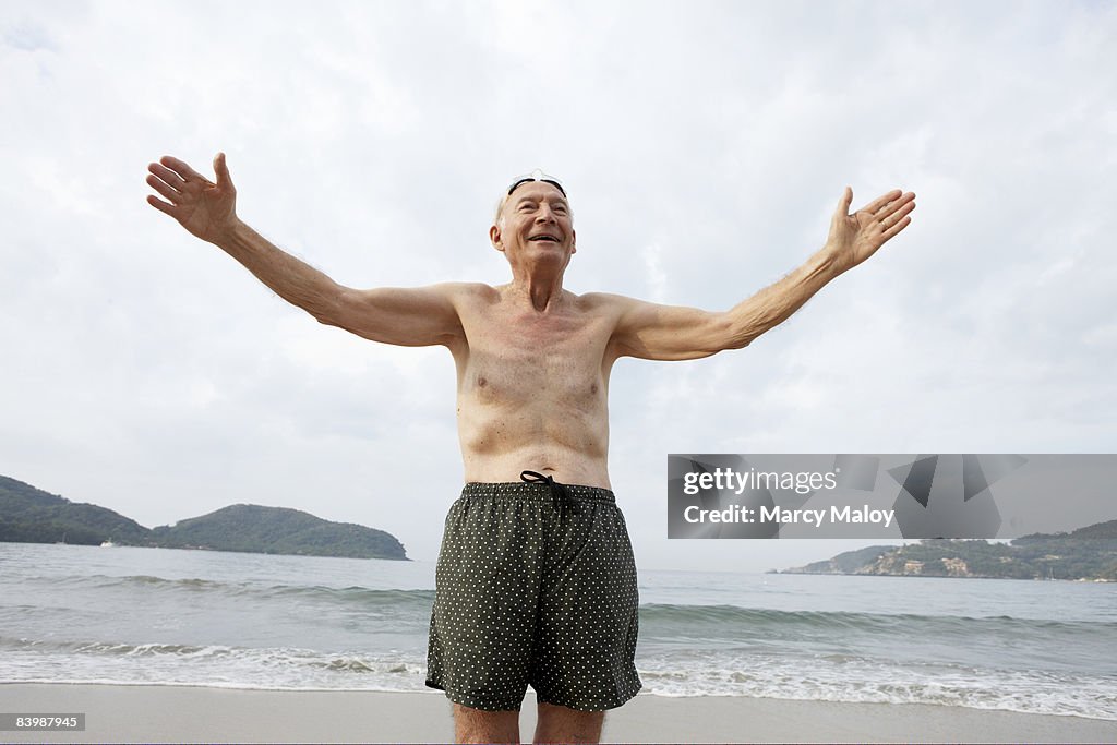 Elderly man in swim trunks on beach  with arms out