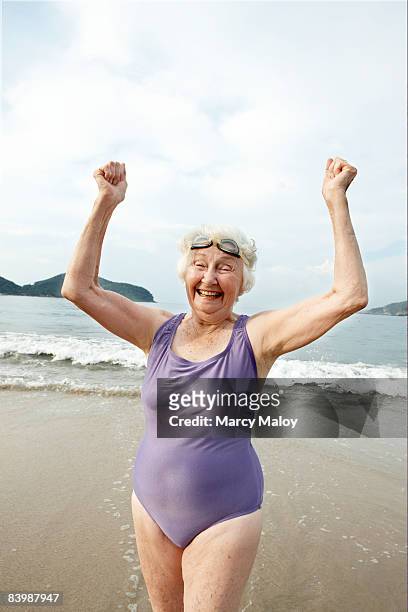 Elderly woman in swimsuit and goggles on beach.   
