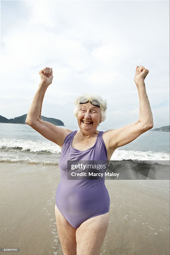 Elderly woman in swimsuit and goggles on beach.