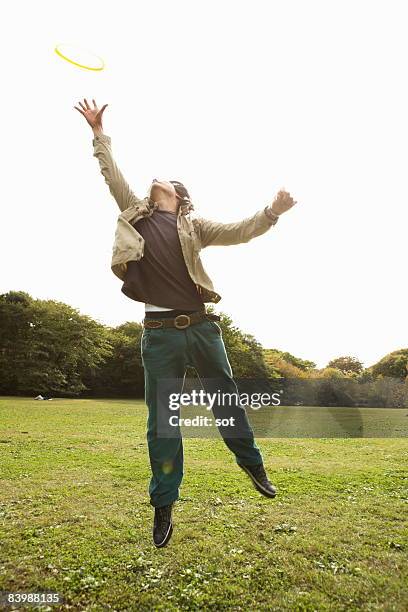 young man jumping for frisbee in the park - frisbee fotografías e imágenes de stock