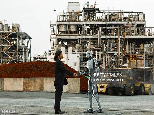 robot and human greeting in front of factory - robô - fotografias e filmes do acervo