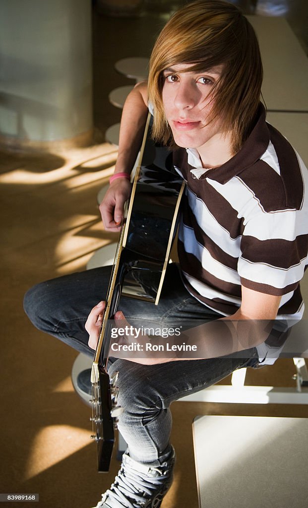 Teen boy practicing guitar in school cafeteria