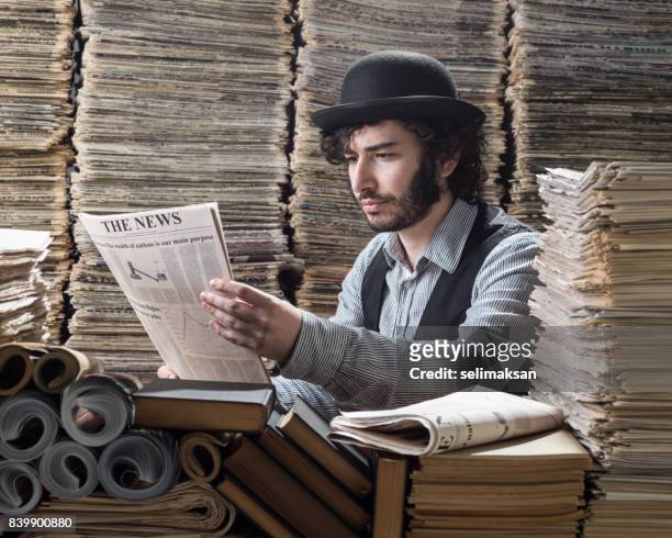young man in old fashioned clothes doing research in printed media library - newspaper stack stock pictures, royalty-free photos & images