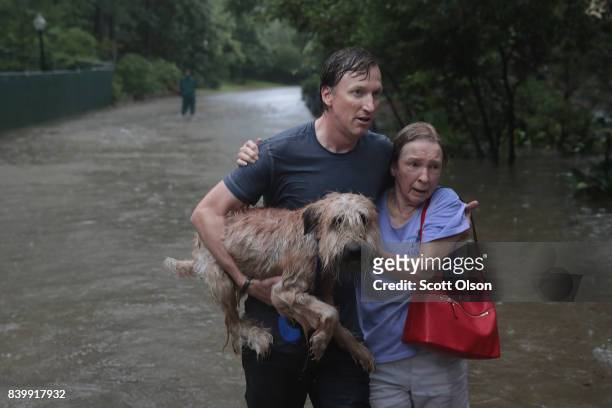 Andrew White helps a neighbor down a street after rescuing her from her home in his boat in the upscale River Oaks neighborhood after it was...