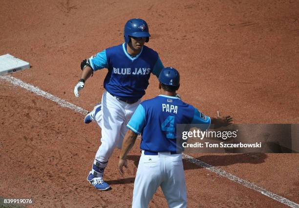 Norichika Aoki of the Toronto Blue Jays is congratulated by third base coach Luis Rivera after hitting a solo home run in the fourth inning during...