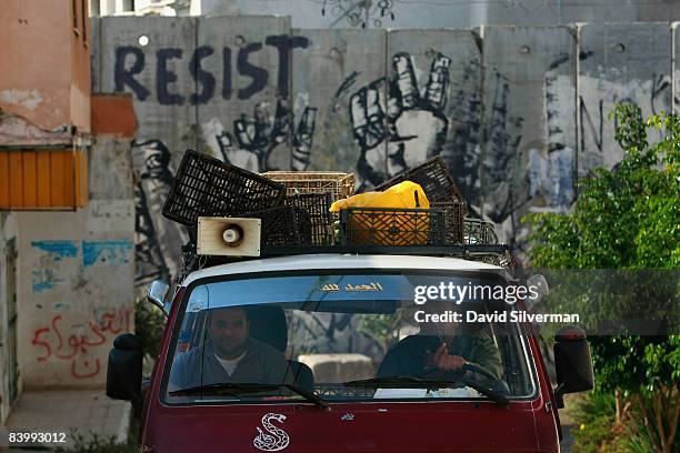 Palestinian farmers selling their produce from the back of a van pass Israel's West Bank separation barrier where it cuts between the Palestinian...