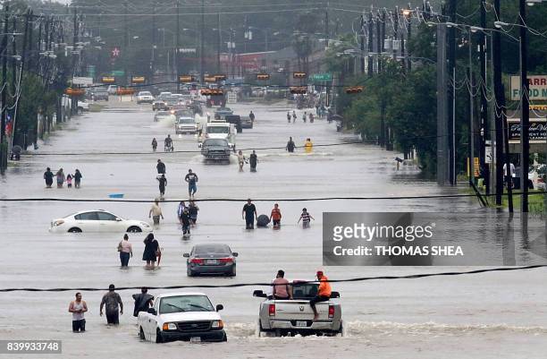 People walk through the flooded waters of Telephone Rd. In Houston on August 27, 2017 as the US fourth city city battles with tropical storm Harvey...