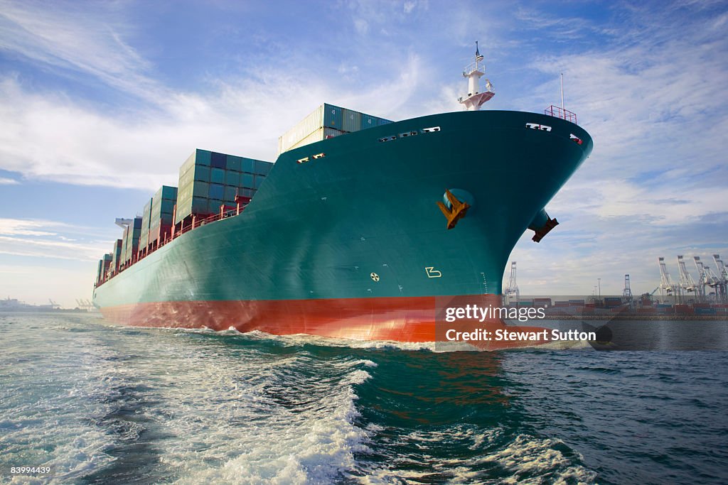 Bow view of loaded cargo ship sailing out of port.