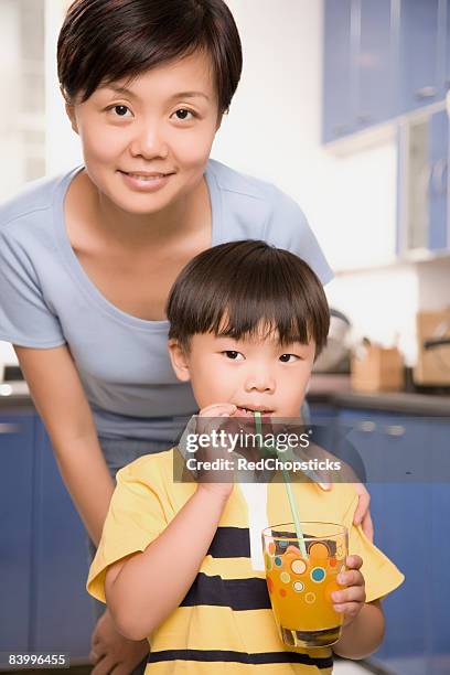close-up of a boy drinking juice with his mother standing behind him - bendy straw stock pictures, royalty-free photos & images