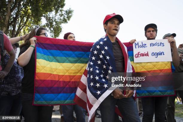 Protester looks on while counter protesters hold a rainbow blanket behind him and a banner reading "Make Racists Afraid Again", during demonstrations...