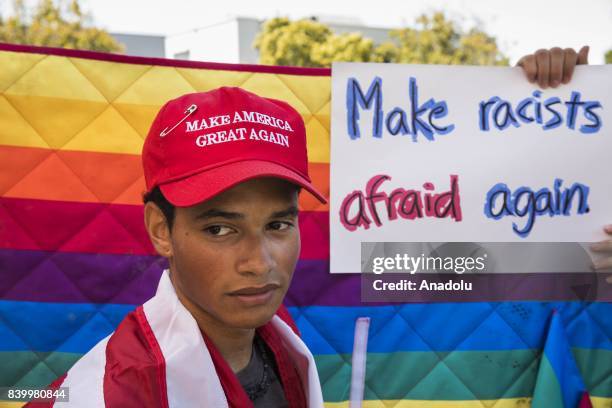 Protester looks on while counter protesters hold a rainbow blanket behind him and a banner reading "Make Racists Afraid Again", during demonstrations...