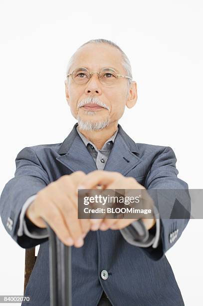 portrait of senior businessman sitting on chair, holding cane, close-up, studio shot - portrait close up loosely stock pictures, royalty-free photos & images