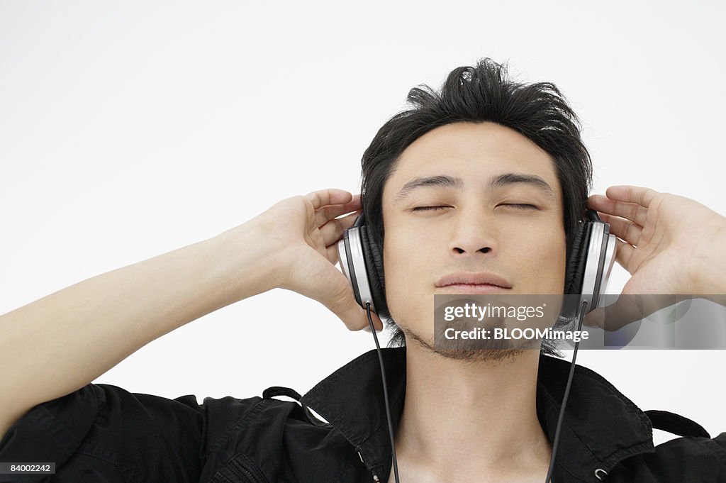 Man listening to music with headphones, eyes closed, studio shot