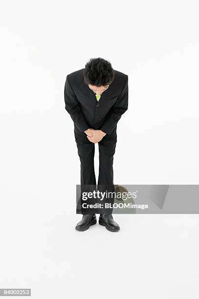 portrait of businessman bowing with hands clasped, studio shot - saluer en s'inclinant photos et images de collection