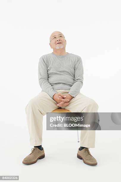 portrait of senior man sitting on chair, clasping hands, studio shot - fatigue full body stock pictures, royalty-free photos & images