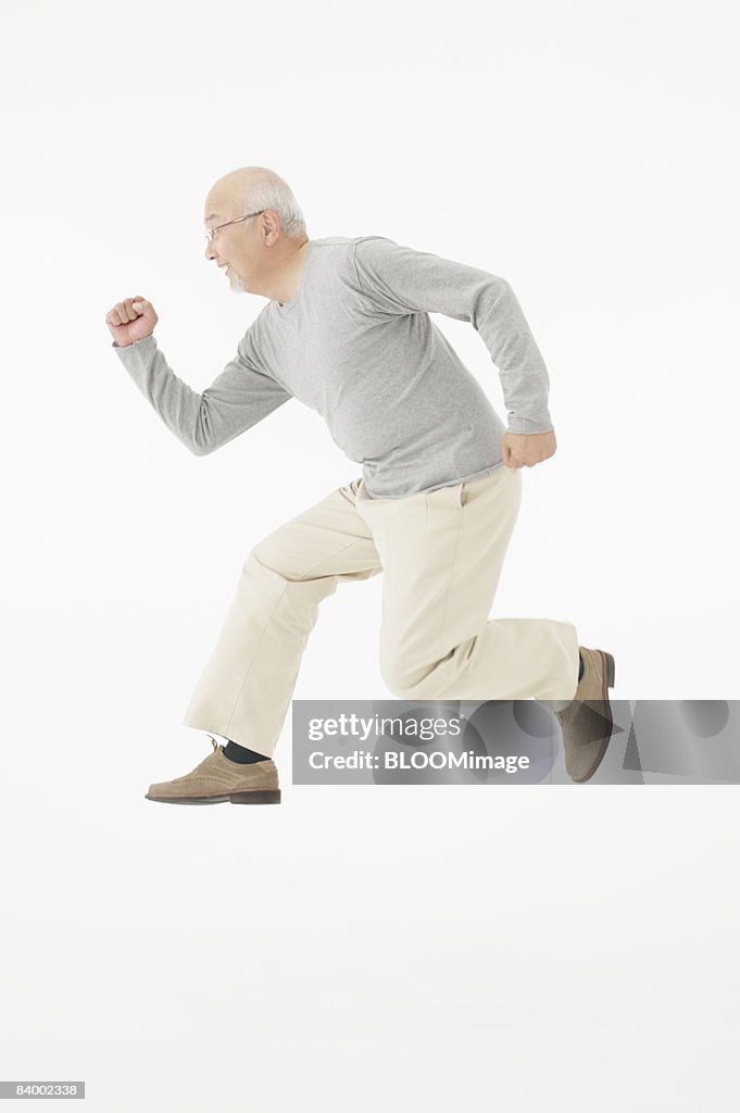 Senior man jumping, clenching fist, side view, studio shot