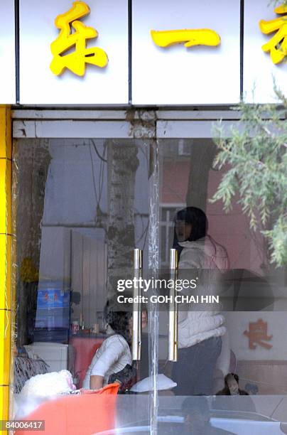 Young Chinese women wait for customers at a barber shop, with the sign saying, "one happiness," in Beijing on December 12, 2008. Hostess bars and...