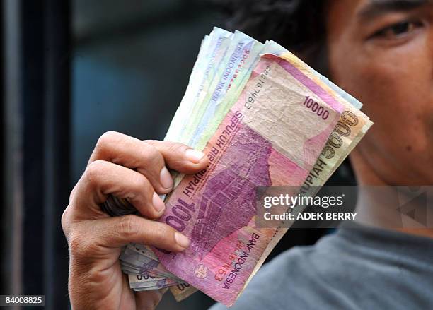 Bus conductor holds up a stack of Indonesian rupiah notes while working in Jakarta on November 20, 2008. Oil and gas companies doing business in...