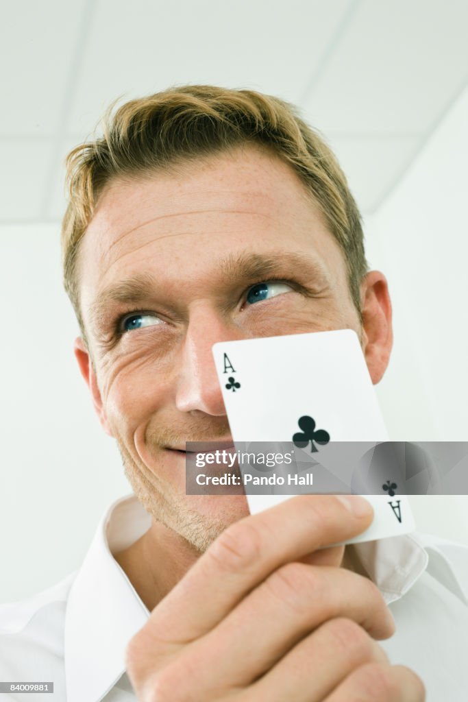 Man holding Ace of clubs playing card, smiling