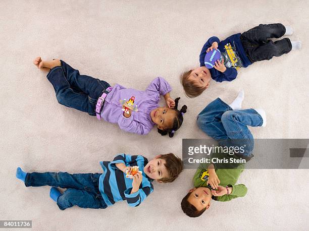 4 yound children playing on a carpet. - lying down stockfoto's en -beelden