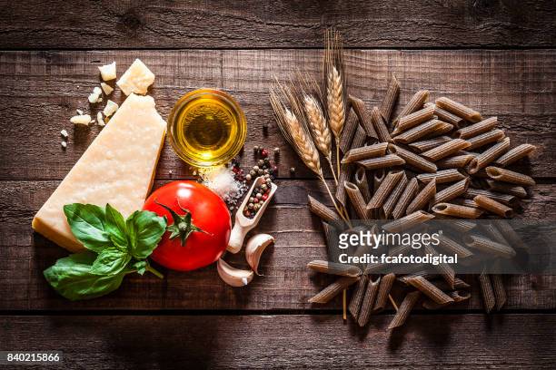 wholegrain penne with ingredients on rustic wooden table - whole wheat penne pasta stock pictures, royalty-free photos & images