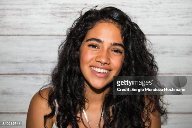 Portrait of one young Hispanic woman smiling at the camera with a white wood background