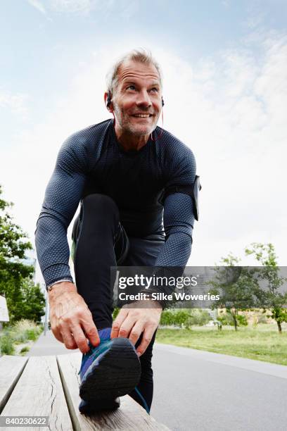 portrait of an active content senior man exercising in a park listening to a podcast - runner warming up stock pictures, royalty-free photos & images