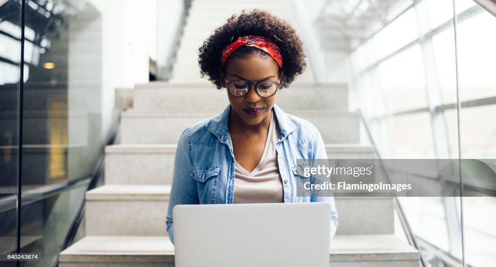 Focused young African student sitting on stairs using a laptop