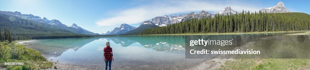 Panoramic of young woman contemplating nature at mountain lake