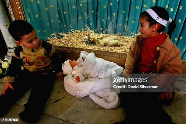 Palestinian Christian children Issa Khader and his sister Adrianne Khader sit alongside their 40-day-old baby brother Riyan Khader who lies in front...