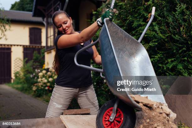 smiling woman disposing old plaster. - wheelbarrow stock-fotos und bilder