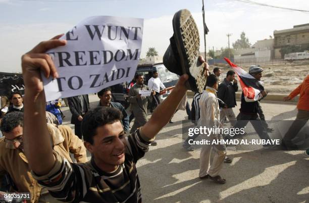 An Iraqi shouts as he holds up a slipper and a sign as they protest against yesterday's visit by US President George W. Bush and the arrest of an...