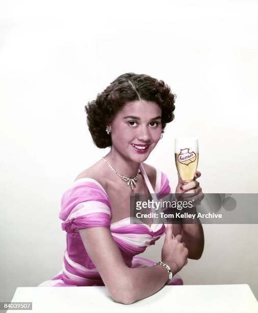 An African American woman smiles and holds up a glass of Falstaff beer in the beer advertisement, 1954. United States.