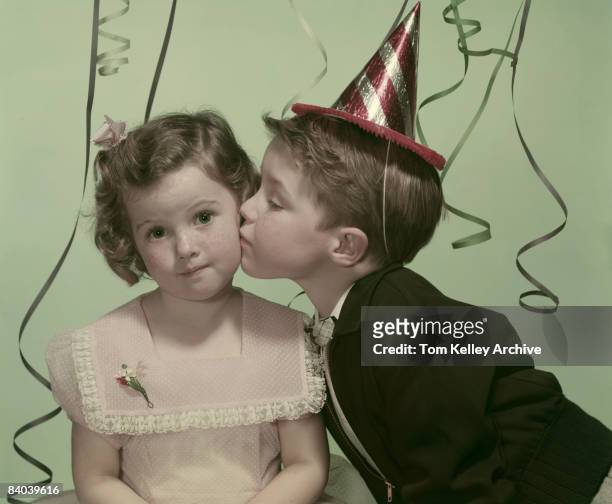 Little boy gives a little girl a peck on the cheek during a birthday party, ca.1950s. United States.