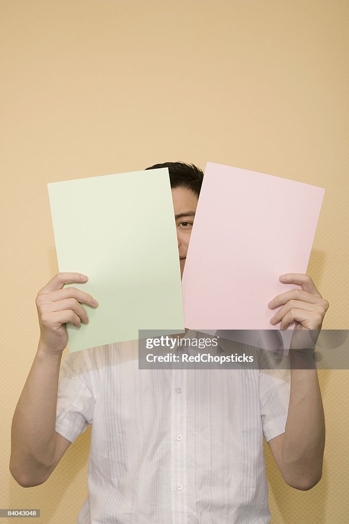 Portrait of a young man peeking through two papers