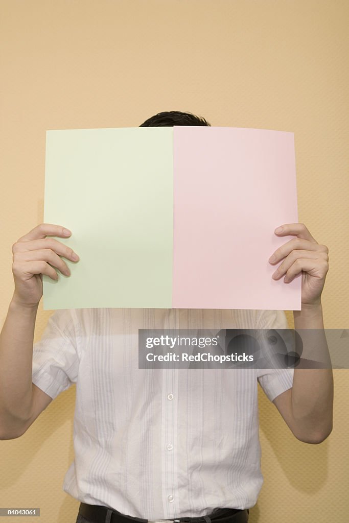 Close-up of a young man hiding his face with papers