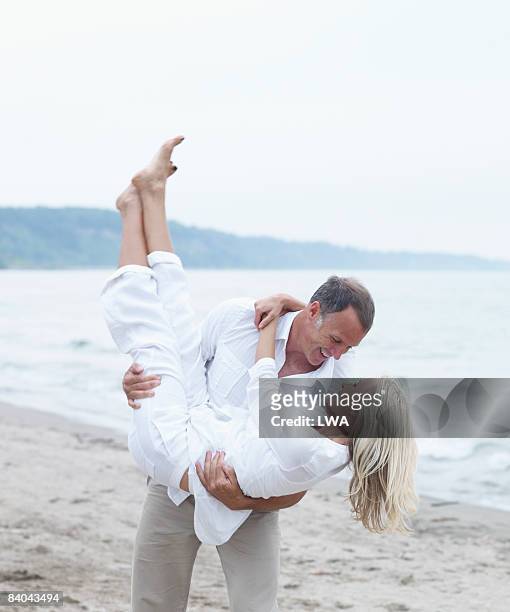 man playfully holding woman on beach - flirt barefoot blonde stock-fotos und bilder