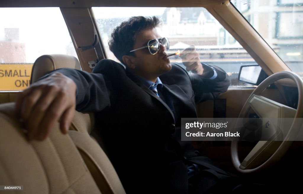 Man wearing suite in a car smoking marijuana