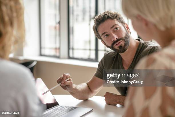 reife geschäftsmann mit bart auf laptop mit bleistift zeigen und kollegen anhören - überzeugen stock-fotos und bilder