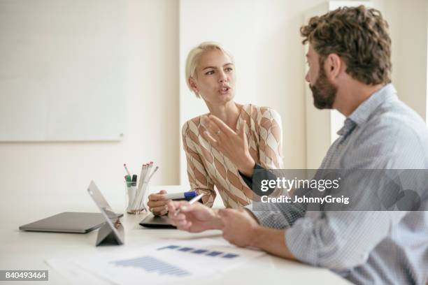 mid adult businesswoman explaining and gesturing to coworker in office - 2 men chatting casual office stock pictures, royalty-free photos & images