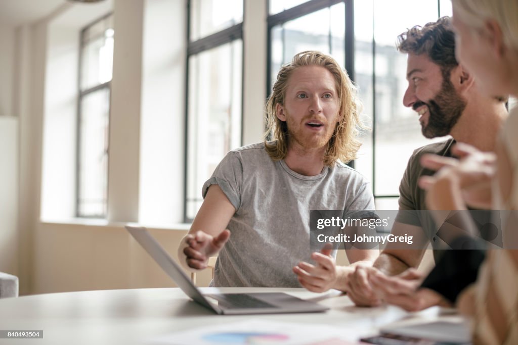 Young creative professional with red wavy hair and beard talking to colleagues