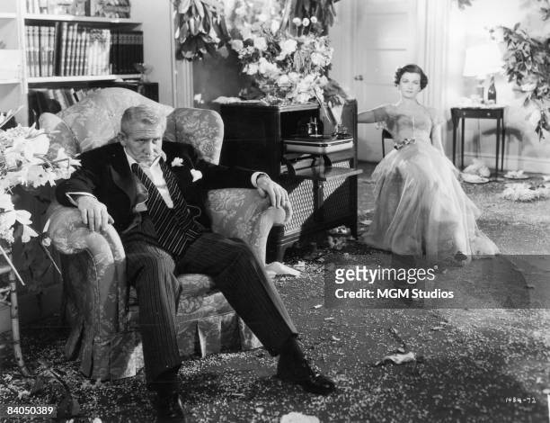 American actors Spencer Tracy and Joan Bennett collapse in separate chairs in a living room littered with confetti in a still from the film 'Father...