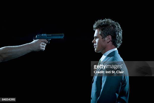 businessman facing hand with gun pointed at head - business revenge stock pictures, royalty-free photos & images