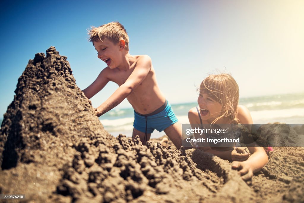 Brother and sister building a sandcastle on beach