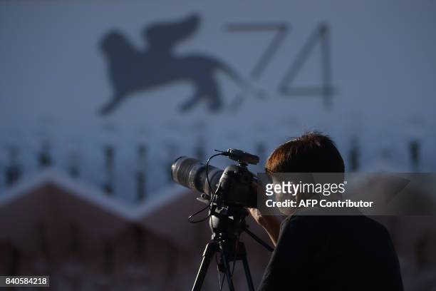 Journalist stands in front of a logo of the 74th Venice Film Festival on August 29, 2017 at Venice Lido on the eve of the opening ceremony. The 74th...
