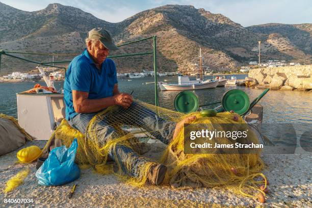 fisherman, mending his nets on the quayside of kamares harbour, sifnos, cyclades islands, greece - sifnos stock-fotos und bilder