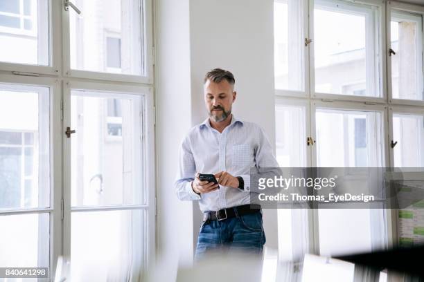 fenster mit smartphone stand büroangestellter - business man looking at smart phone stock-fotos und bilder