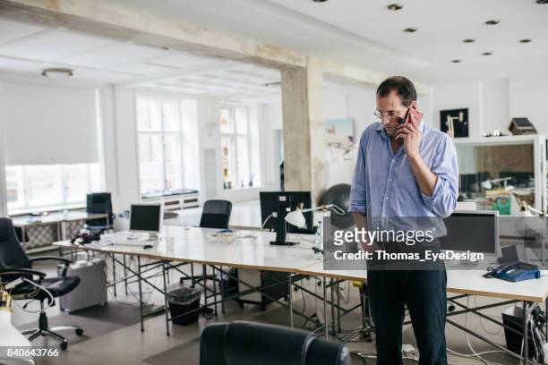 manager talking on smartphone in empty office space - empty office one person stock pictures, royalty-free photos & images